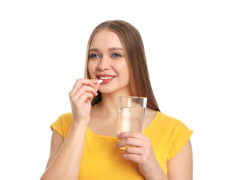 Photo of Young woman with glass of water taking vitamin pill on white background