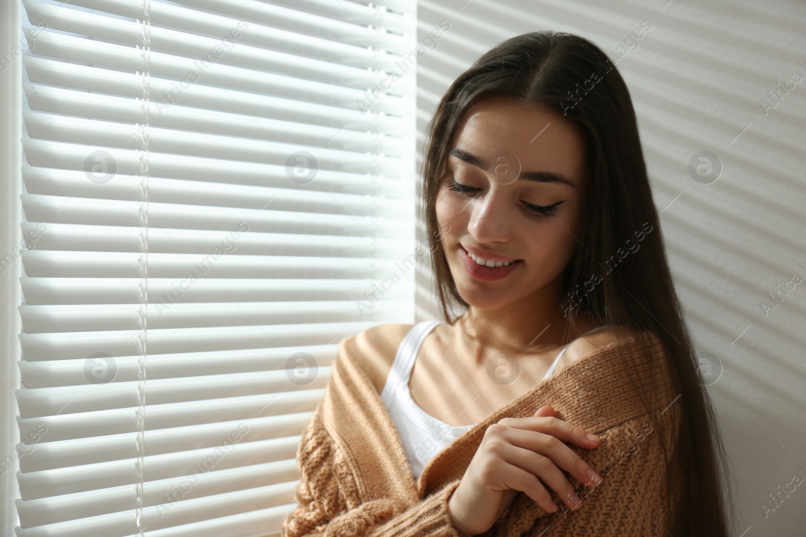 Photo of Young woman near window with Venetian blinds. Space for text