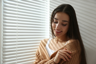 Young woman near window with Venetian blinds. Space for text