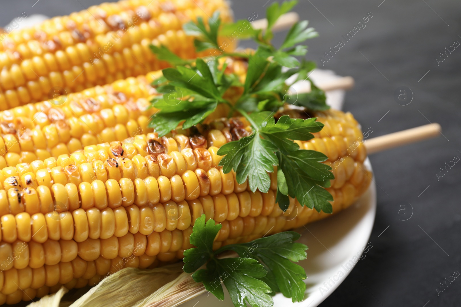 Photo of Tasty grilled corn on black table, closeup