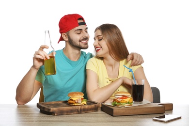 Happy couple having lunch with burgers at table on white background