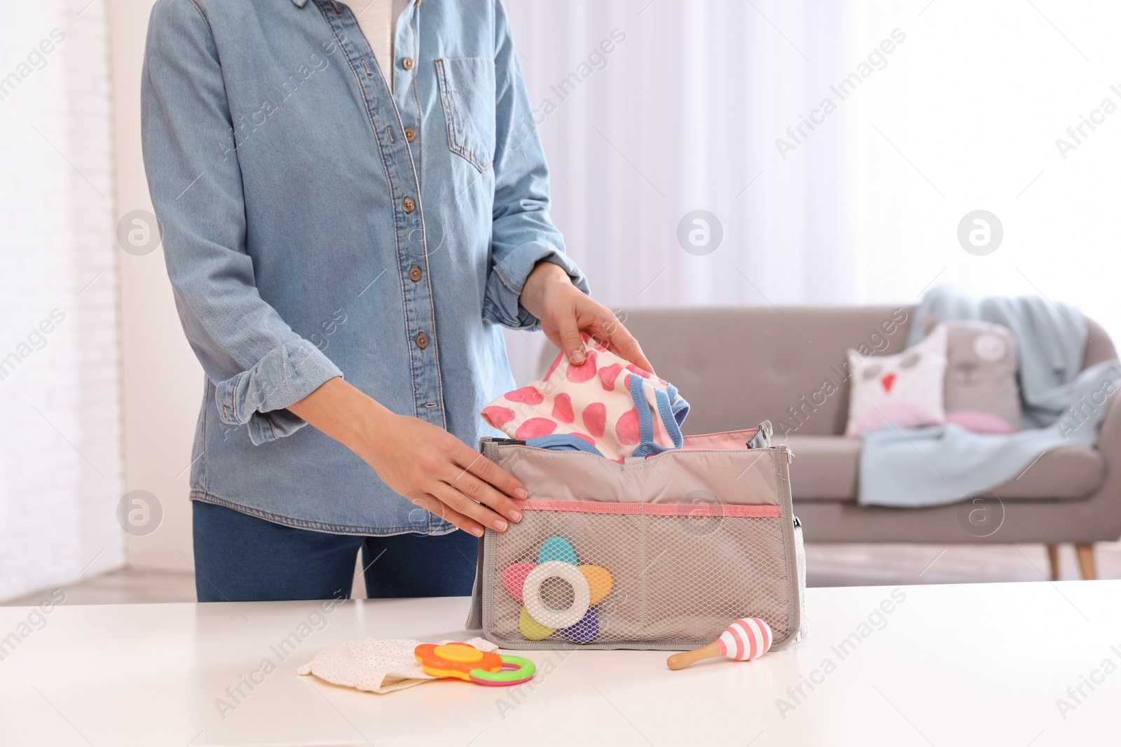 Photo of Woman packing baby accessories into maternity bag on table indoors, closeup