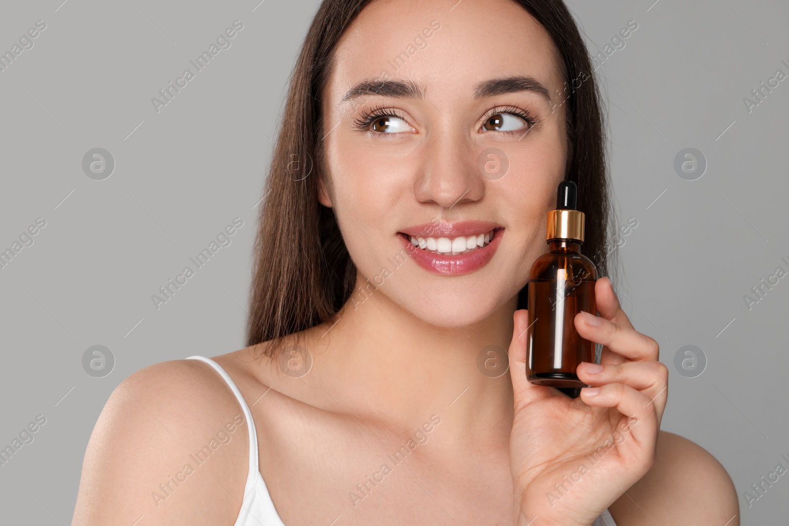 Photo of Beautiful young woman with bottle of essential oil on light grey background