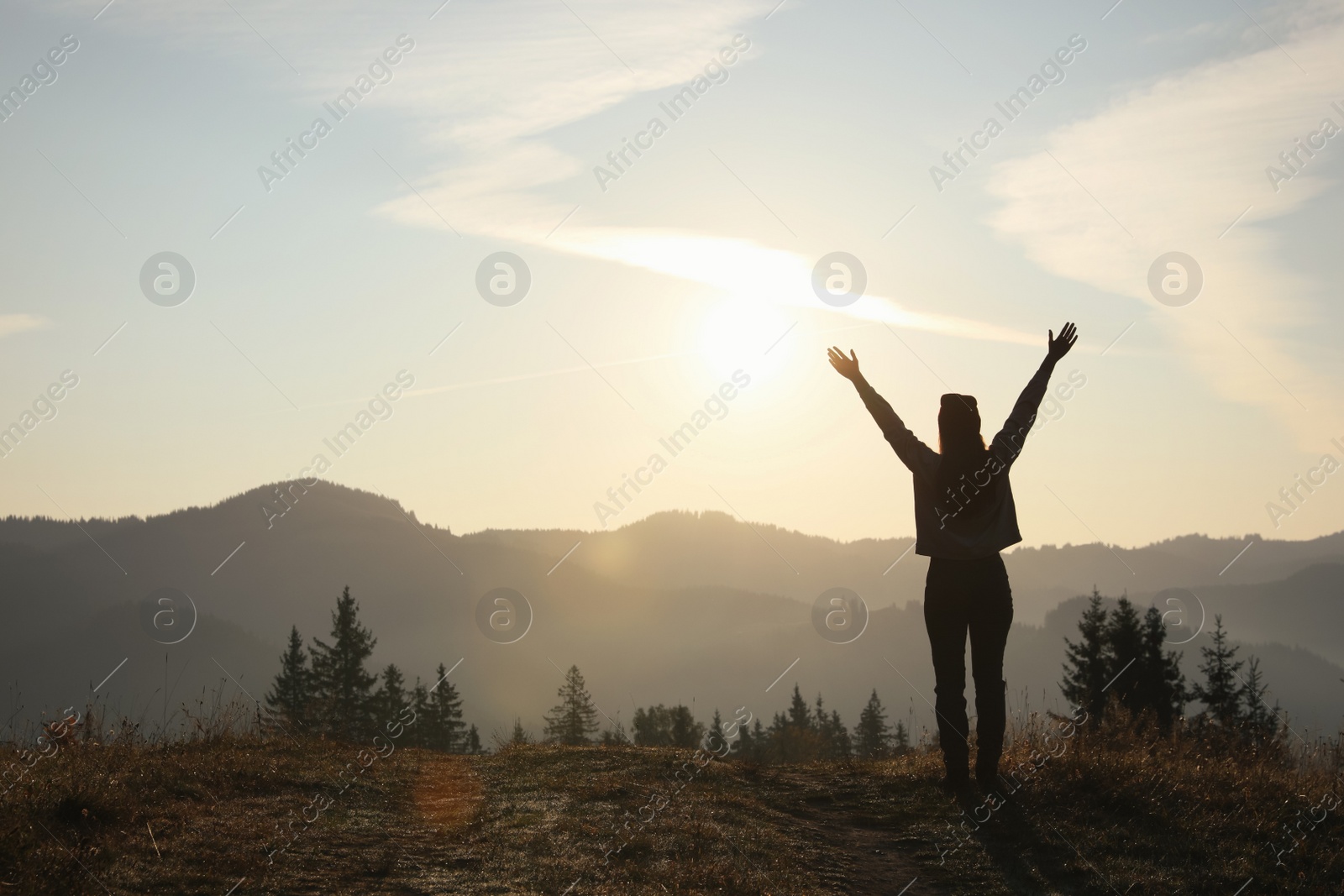 Photo of Silhouette of woman at sunrise in mountains, back view. Space for text