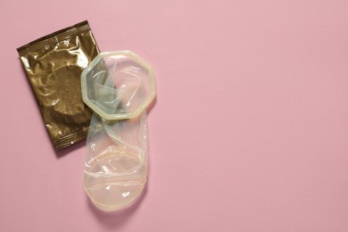 Unrolled female condom and package on light pink background, flat lay with space for text. Safe sex