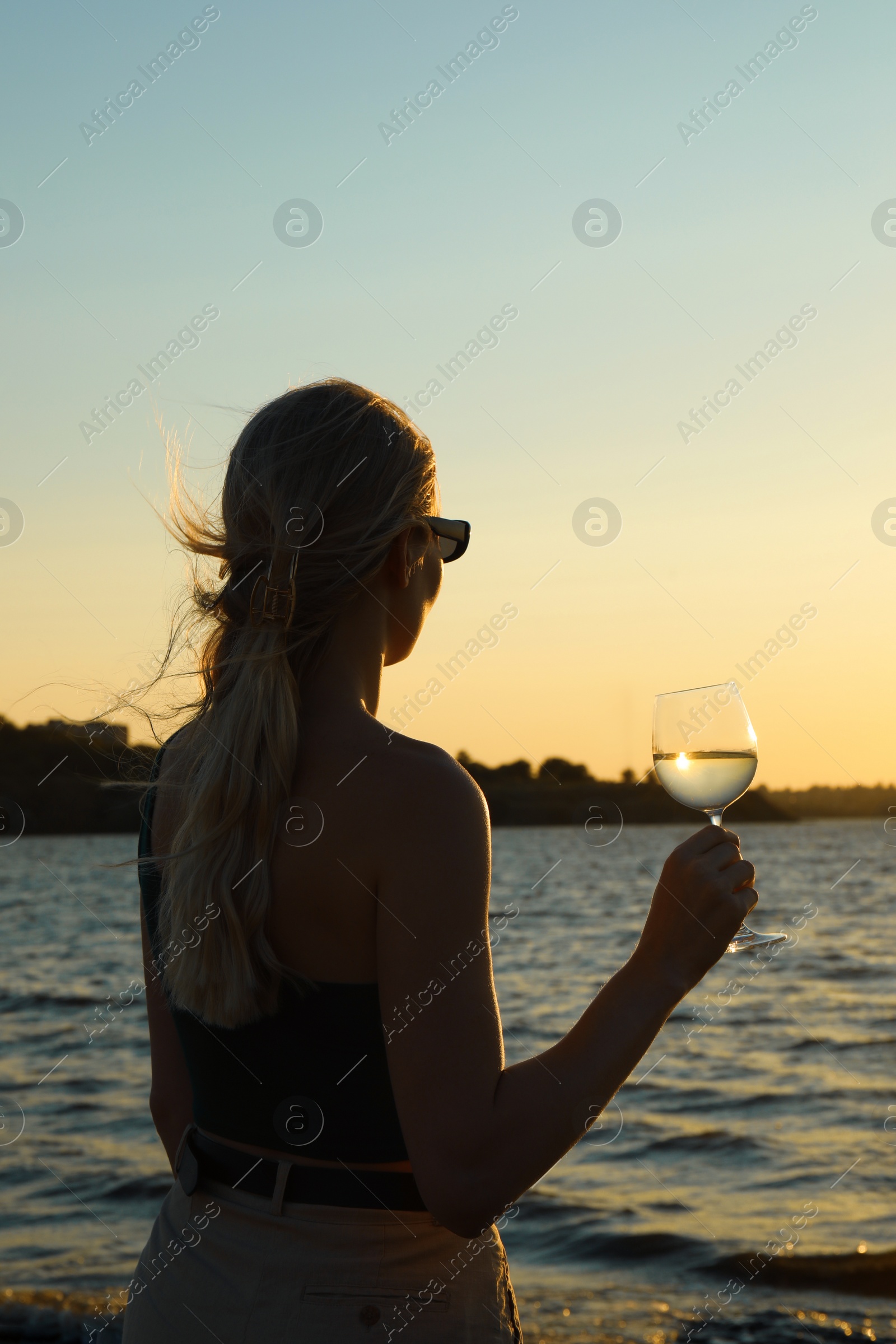 Photo of Woman with glass of wine near sea at sunset