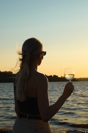 Woman with glass of wine near sea at sunset