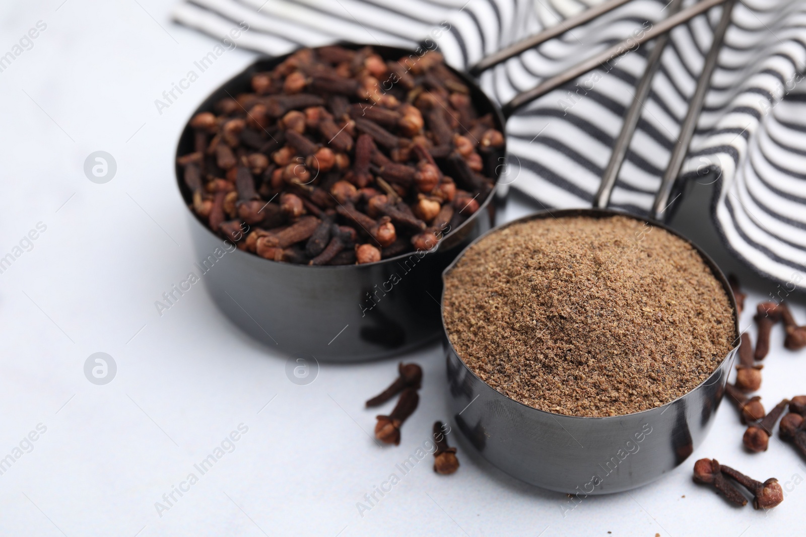 Photo of Aromatic clove powder and dried buds in scoops on white table, closeup