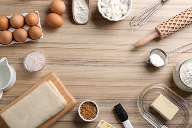 Frame made with puff pastry dough and ingredients on wooden table, flat lay. Space for text