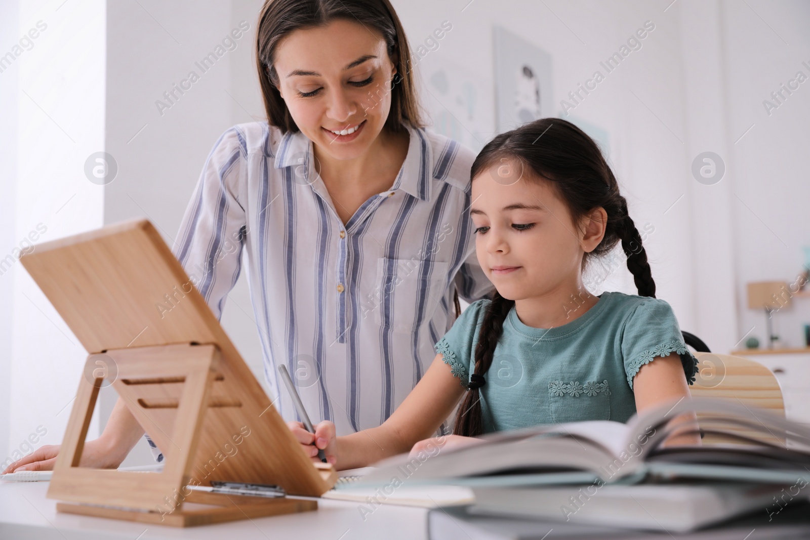 Photo of Mother helping her daughter doing homework with tablet at home