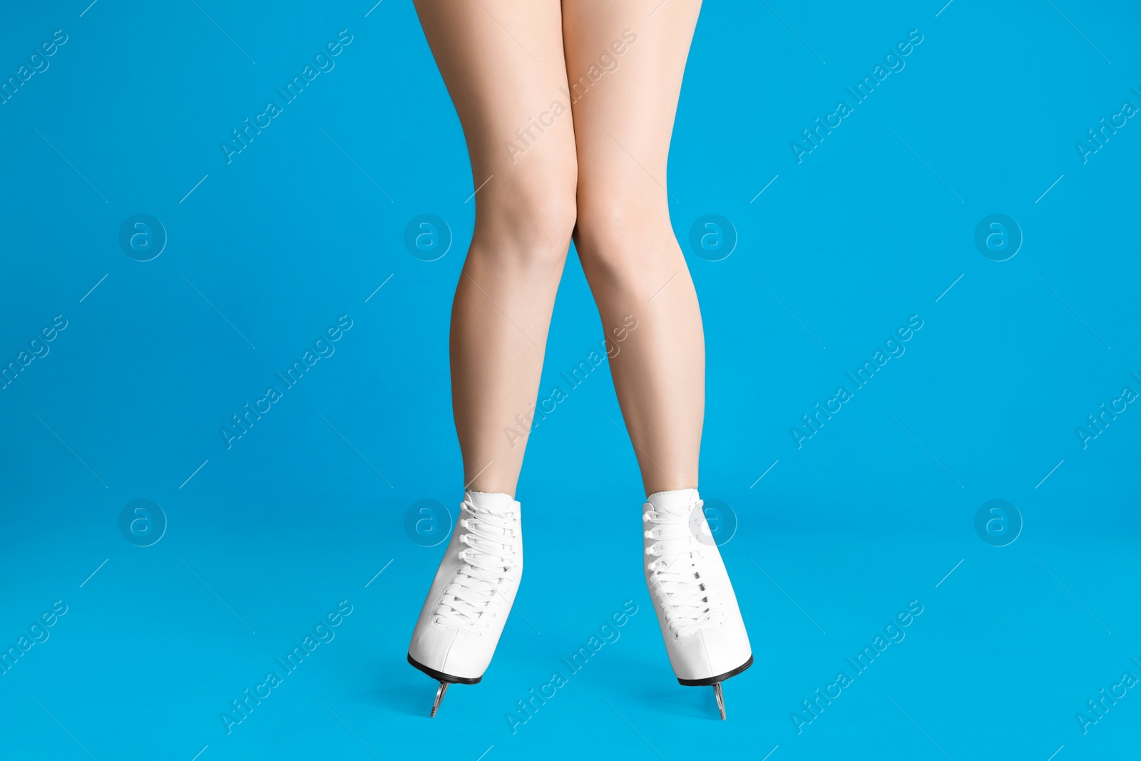 Photo of Woman in elegant white ice skates on light blue background, closeup of legs