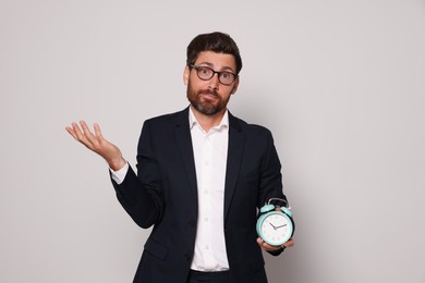 Emotional bearded man with alarm clock on light grey background. Being late concept