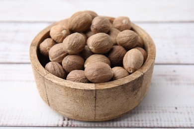 Photo of Whole nutmegs in bowl on light wooden table, closeup
