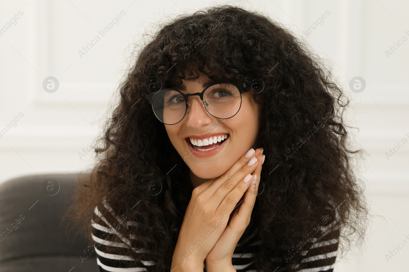 Photo of Portrait of beautiful woman with curly hair sitting on armchair indoors. Attractive lady smiling and looking at camera