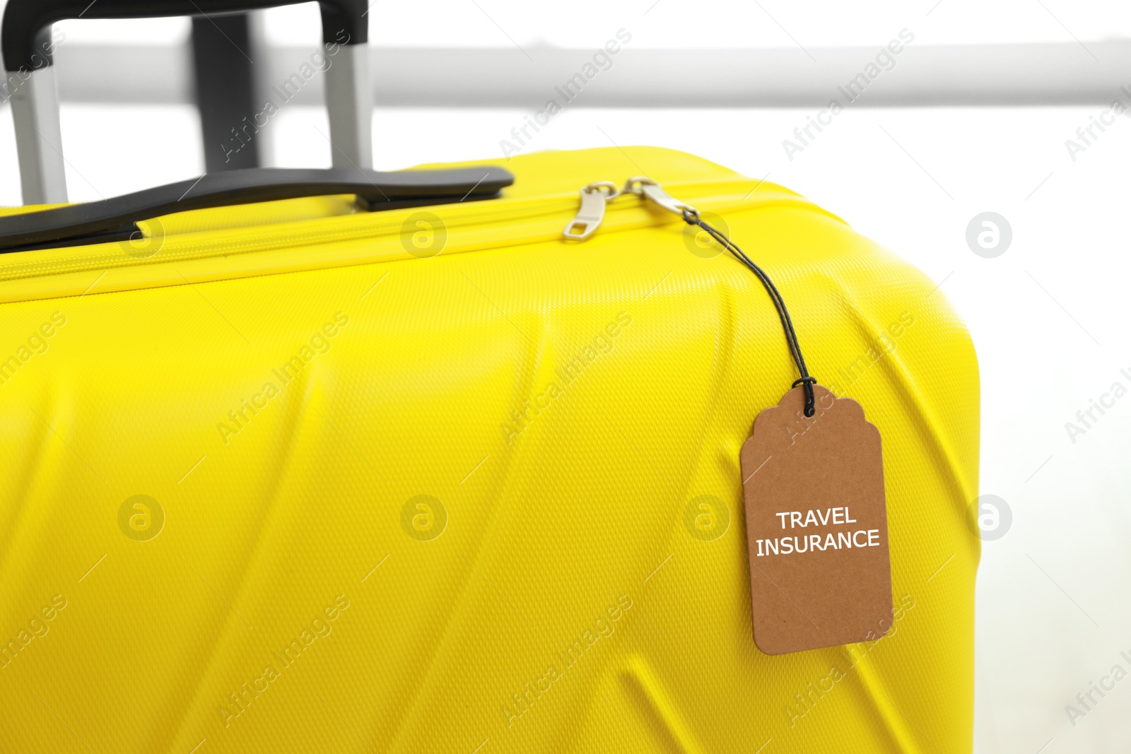 Photo of Yellow suitcase with TRAVEL INSURANCE label indoors, closeup