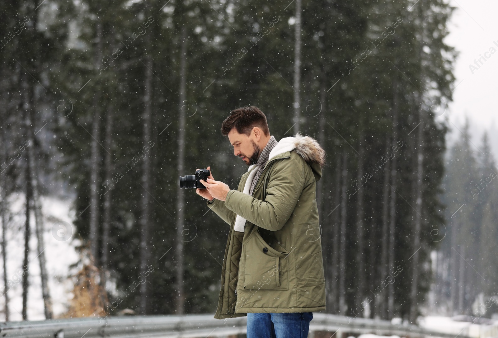 Photo of Man with camera walking near forest on snowy winter day