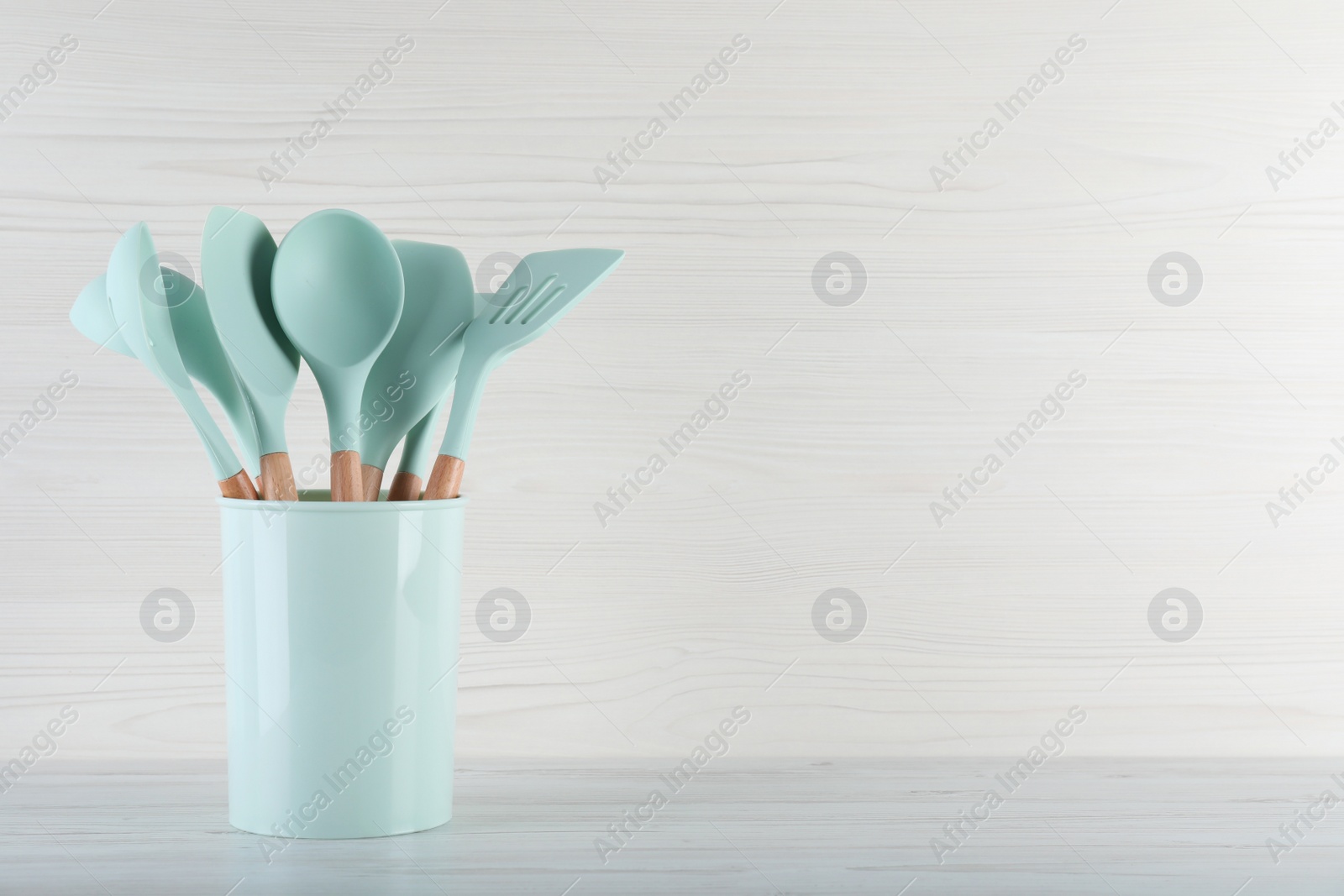 Photo of Holder with different kitchen utensils on white wooden table. Space for text