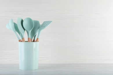 Photo of Holder with different kitchen utensils on white wooden table. Space for text