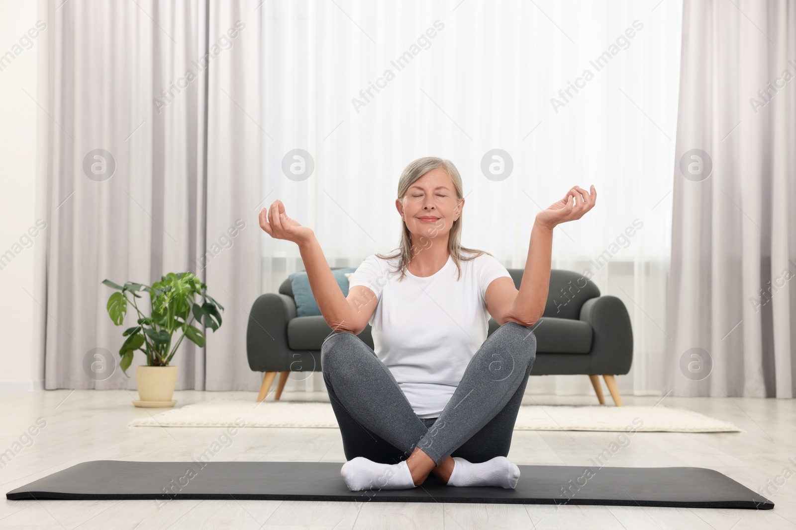 Photo of Happy senior woman practicing yoga on mat at home