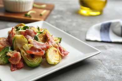 Photo of Delicious roasted Brussels sprouts with bacon served on grey table, closeup