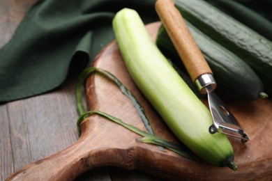 Photo of Fresh cucumbers and peeler on wooden table, closeup