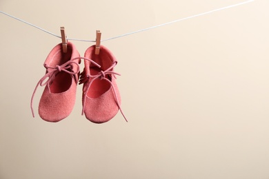 Photo of Cute small shoes hanging on washing line against color background, space for text. Baby accessories