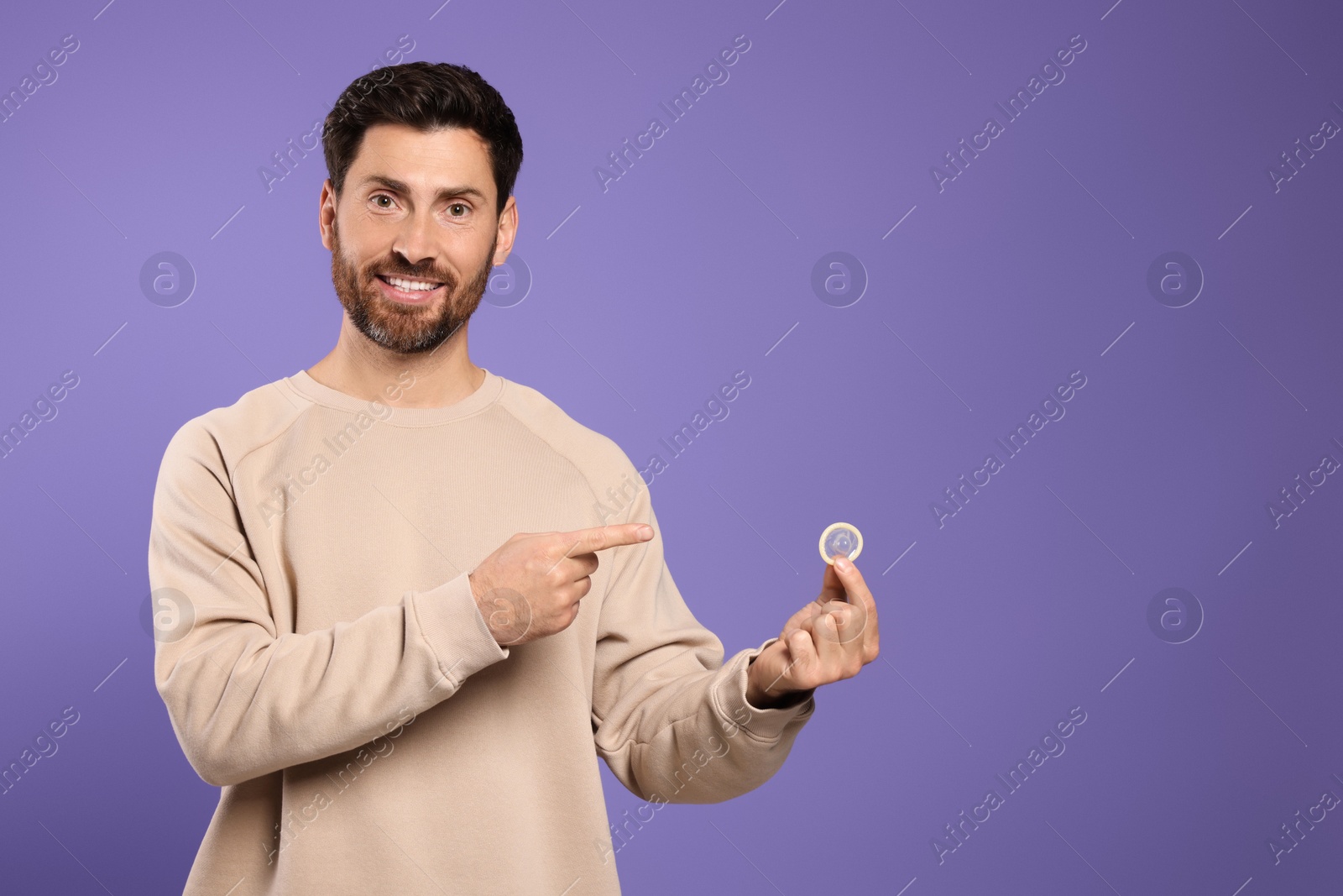 Photo of Man holding condom on purple background, space for text. Safe sex