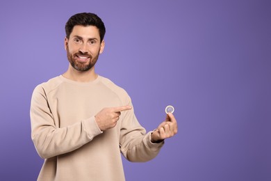 Photo of Man holding condom on purple background, space for text. Safe sex