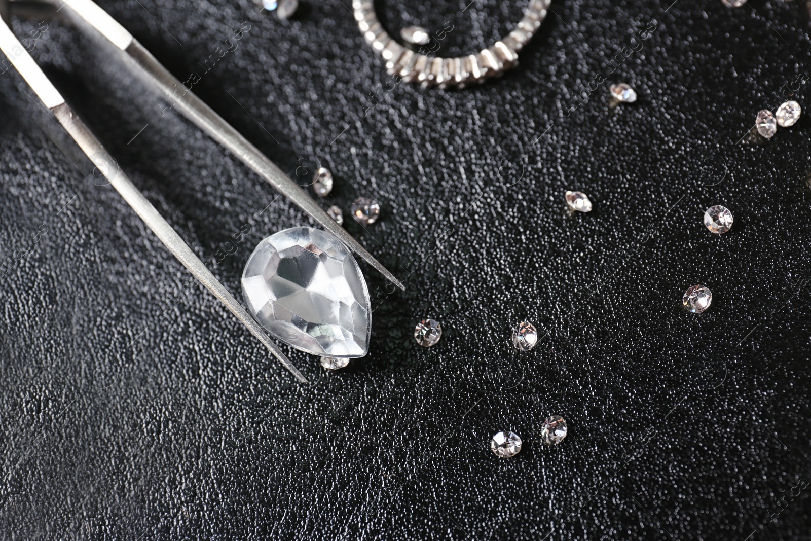 Photo of Jewels and tweezers on black leather surface