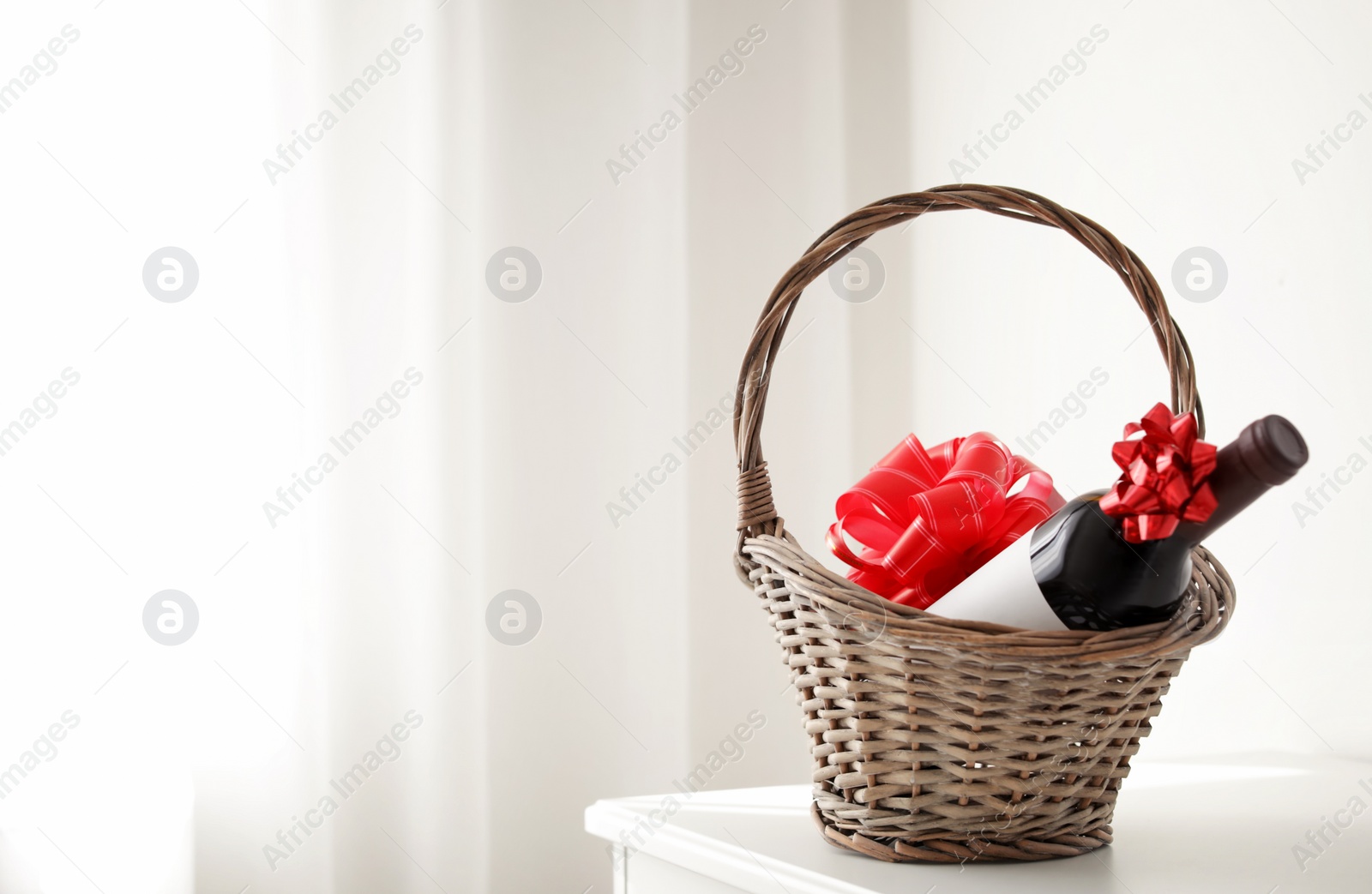 Photo of Wicker basket with bottle of wine on table in light room. Space for text