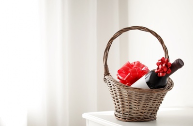 Wicker basket with bottle of wine on table in light room. Space for text