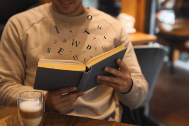 Image of Man with coffee reading book with letters flying over it at wooden table, closeup