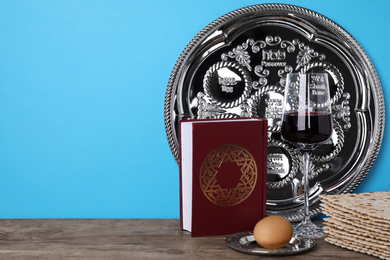 Photo of Symbolic Pesach (Passover Seder) items on wooden table against blue background, space for text
