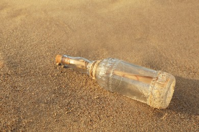 Photo of SOS message in glass bottle on sand, closeup