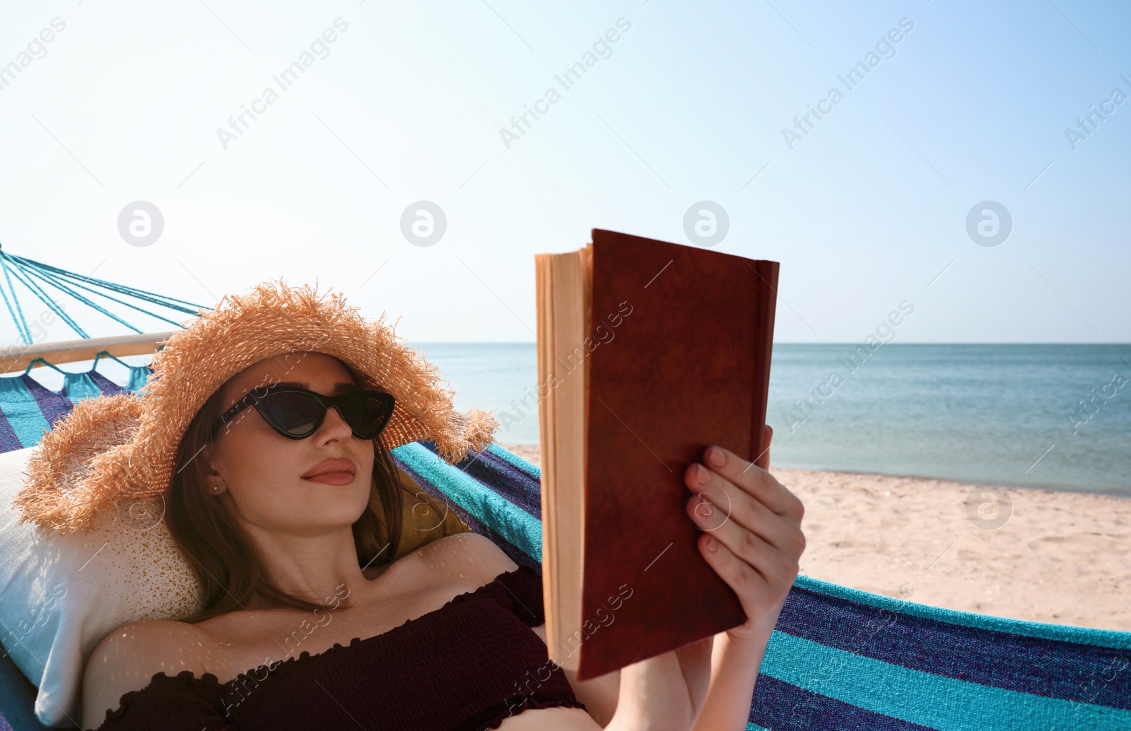 Photo of Young woman reading book in hammock on beach