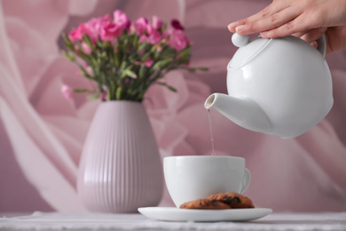 Photo of Woman pouring hot tea into cup at table, closeup