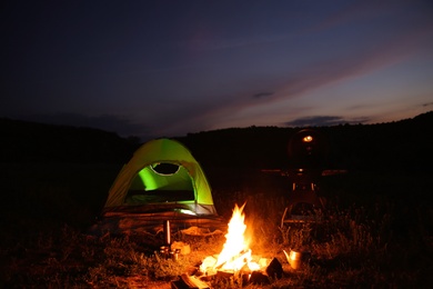 Camping tent near small bonfire at night