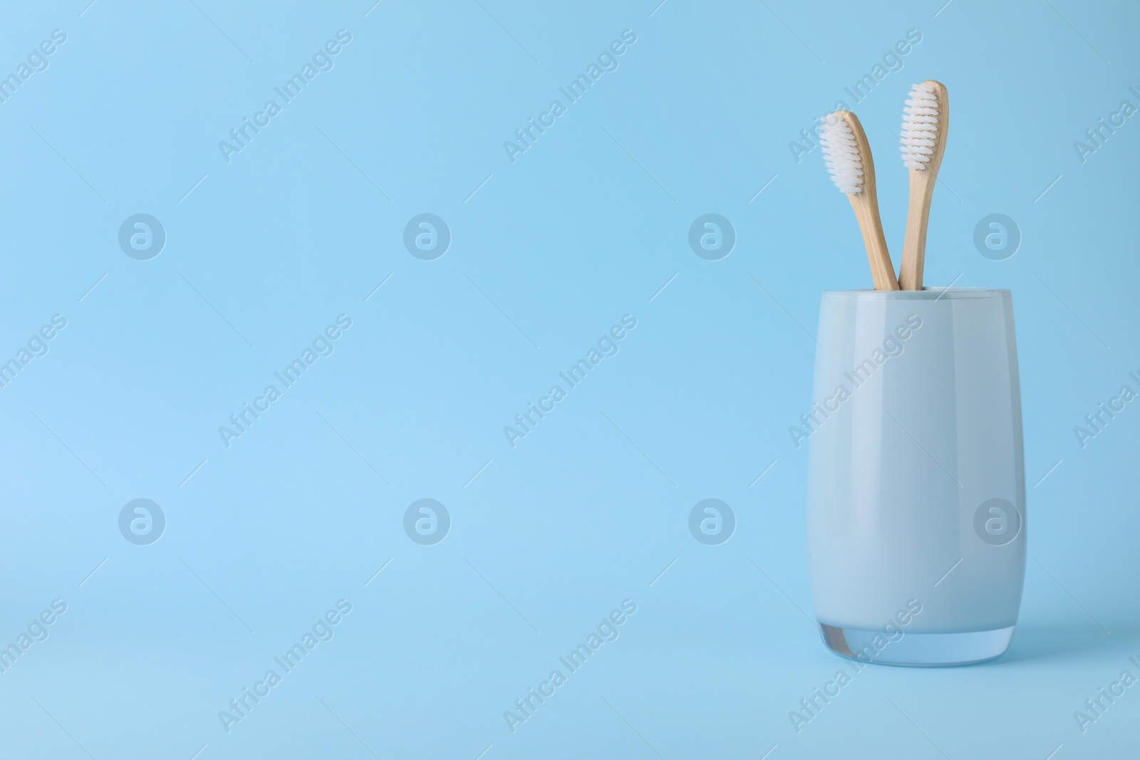 Photo of Bamboo toothbrushes in holder on light blue background, space for text