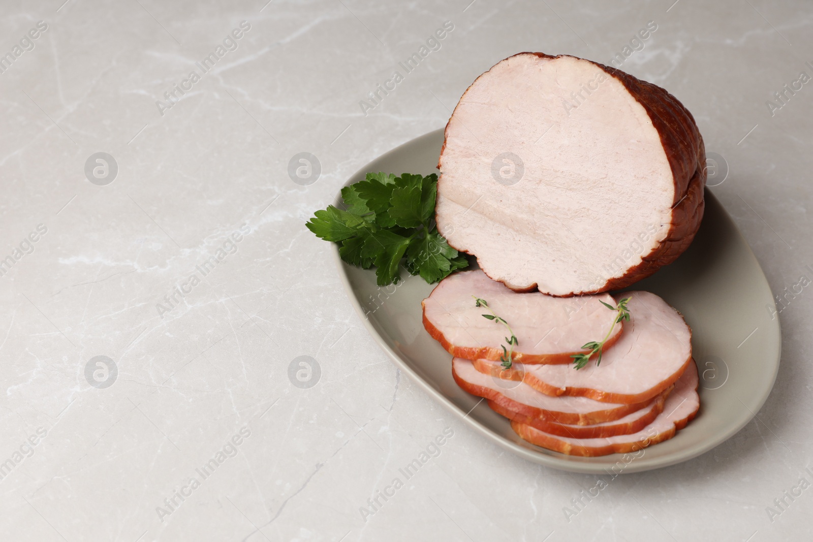 Photo of Delicious cut ham with aromatic herbs on light grey table, space for text