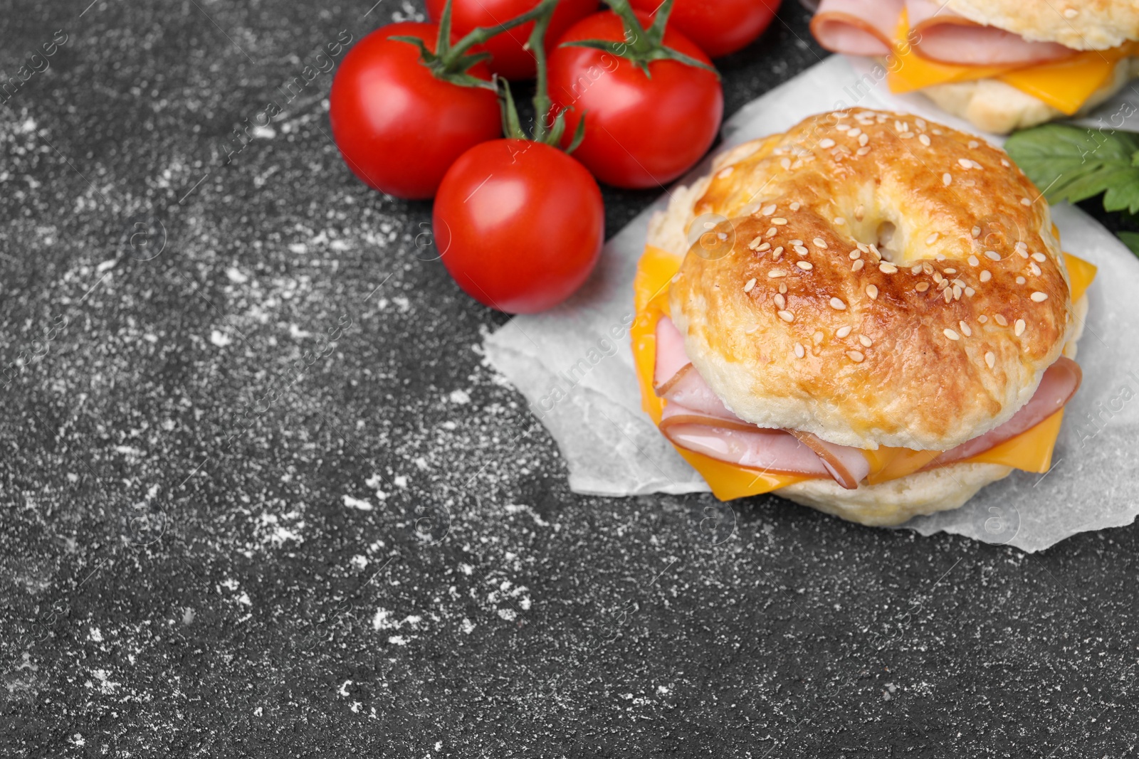 Delicious bagels with ham, cheese and products on dark grey textured table, space for text Photo of Delicious bagels with ham, cheese and products on dark grey textured table, space for text
