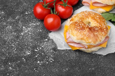 Photo of Delicious bagels with ham, cheese and products on dark grey textured table, space for text
