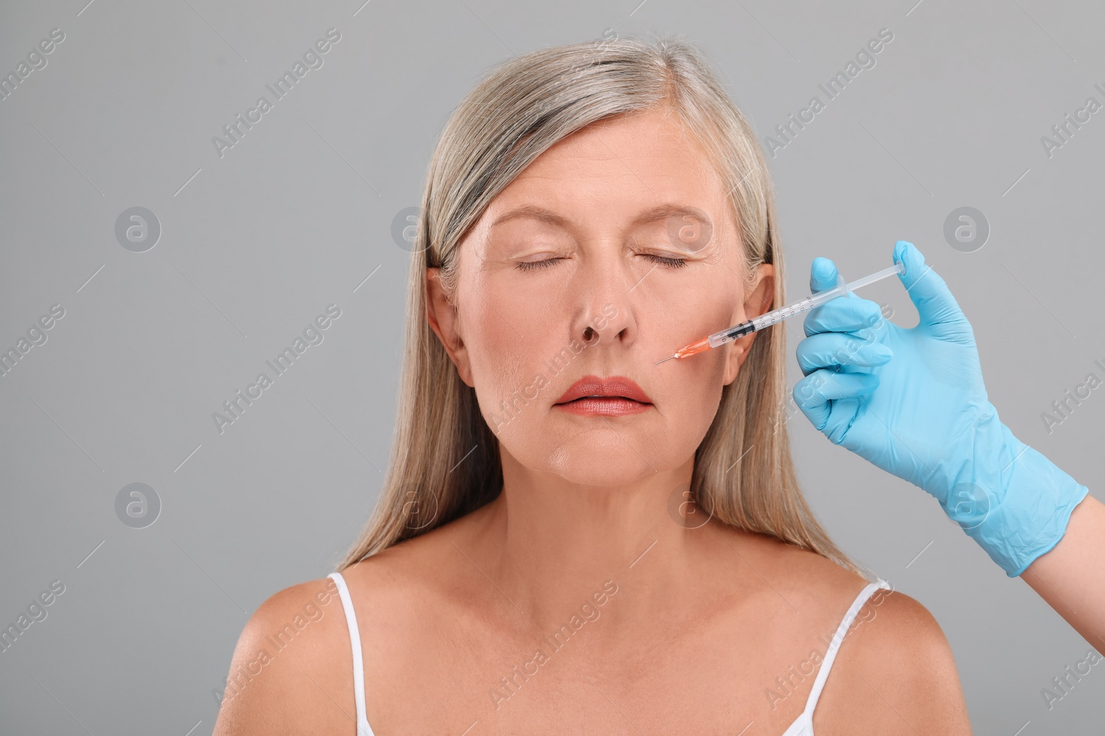 Photo of Doctor giving facial injection to senior woman on light grey background, closeup. Cosmetic surgery