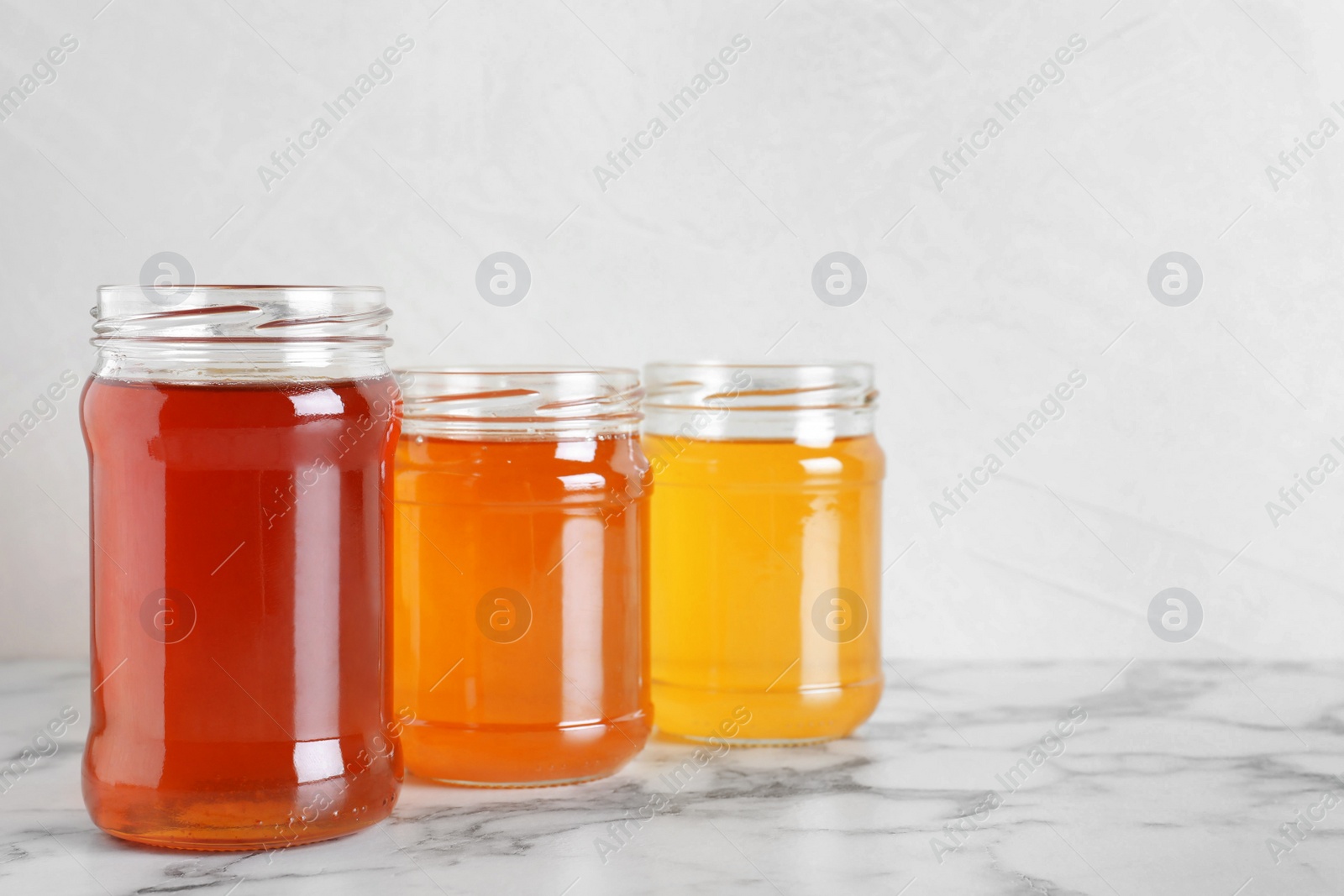 Photo of Jars with different types of organic honey on marble table against white background
