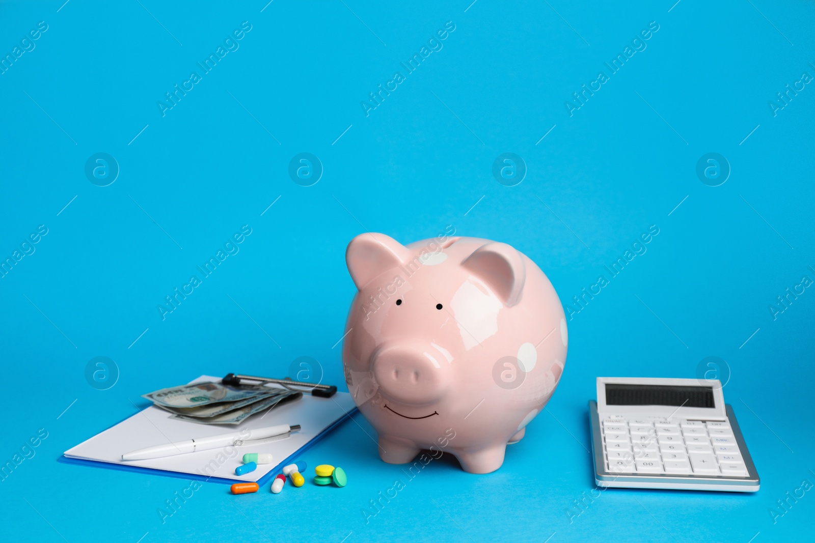Photo of Pale pink ceramic piggy bank, clipboard and calculator on light blue background. Medical insurance