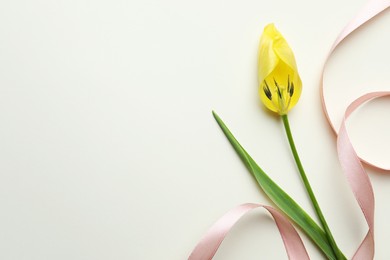 Photo of Yellow tulip and pink ribbon on beige background, top view with space for text. Menopause concept