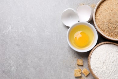 Fresh breadcrumbs, flour and egg on light grey table, flat lay. Space for text