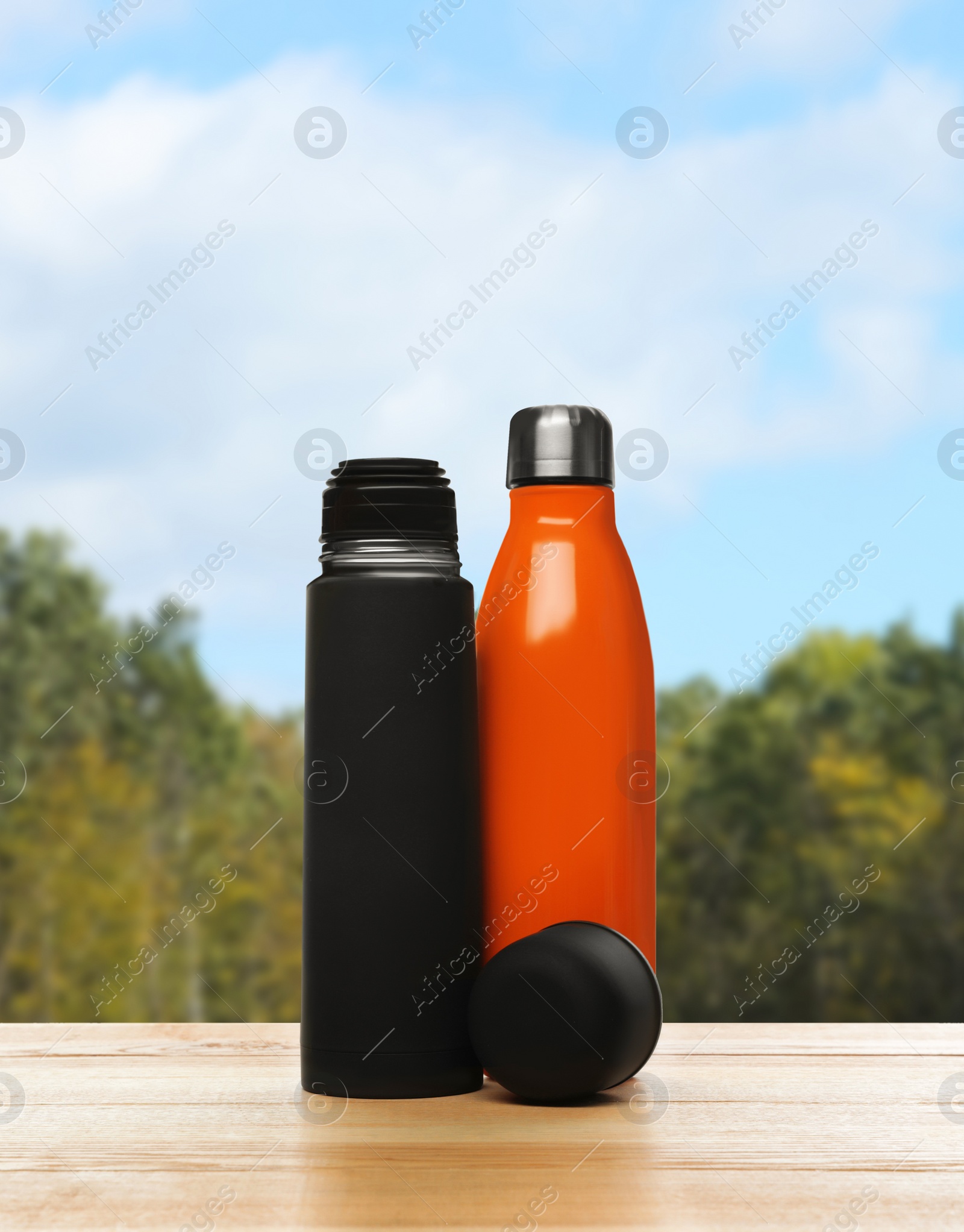 Image of Thermos bottles on wooden table against blurred forest