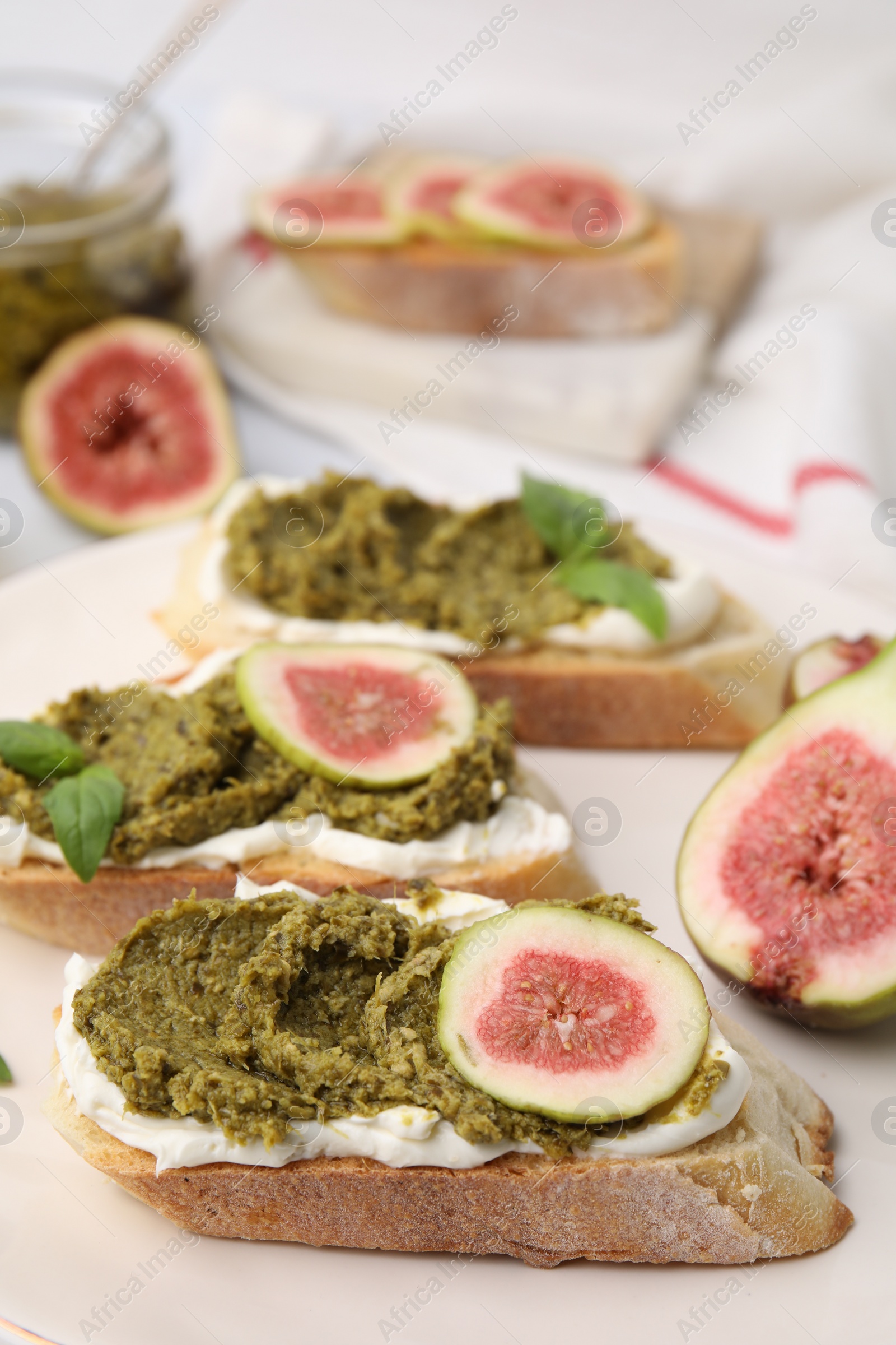 Photo of Tasty bruschettas with cream cheese, pesto sauce, figs and fresh basil on plate, closeup