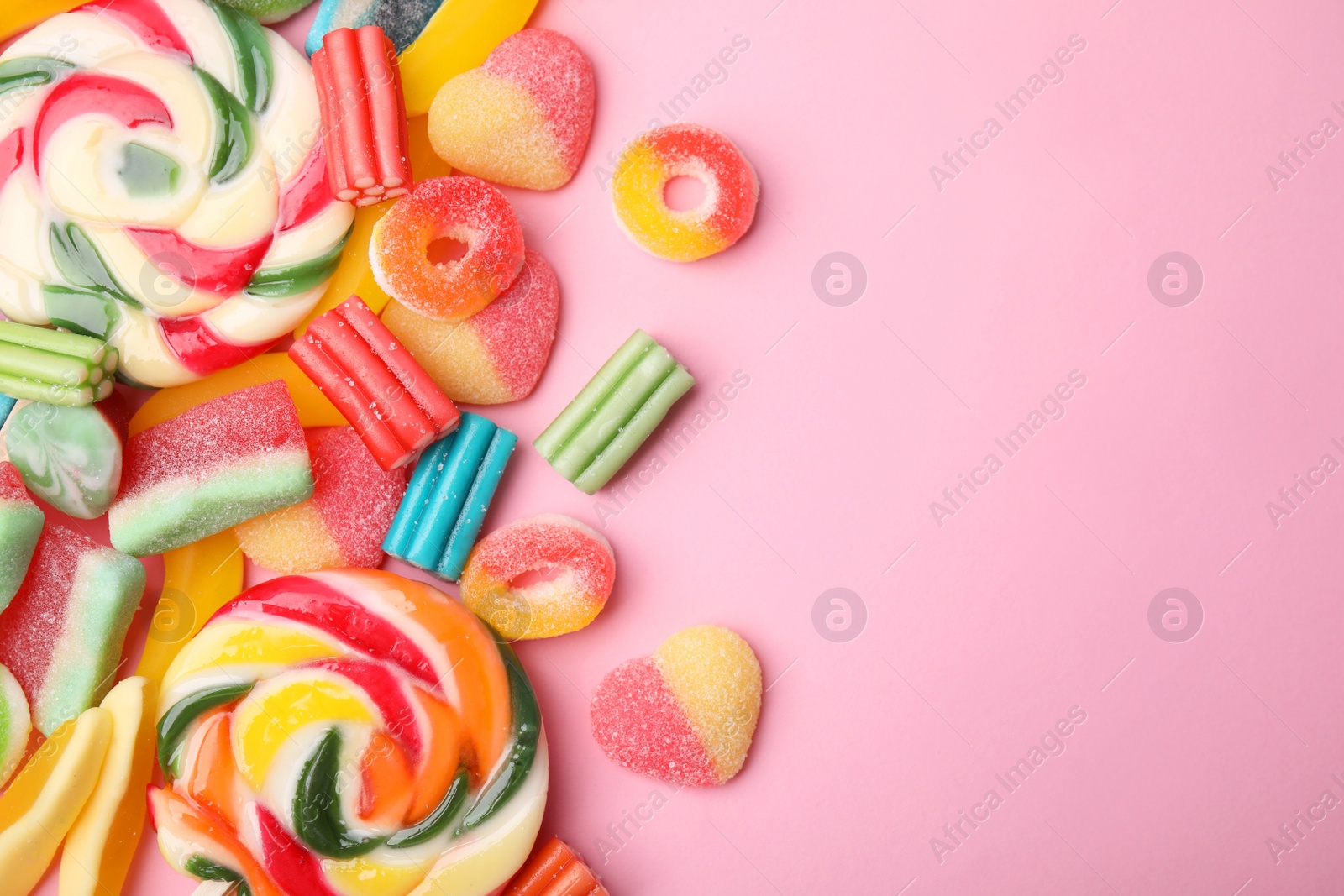 Photo of Many different jelly candies and lollipops on pink background, flat lay. Space for text