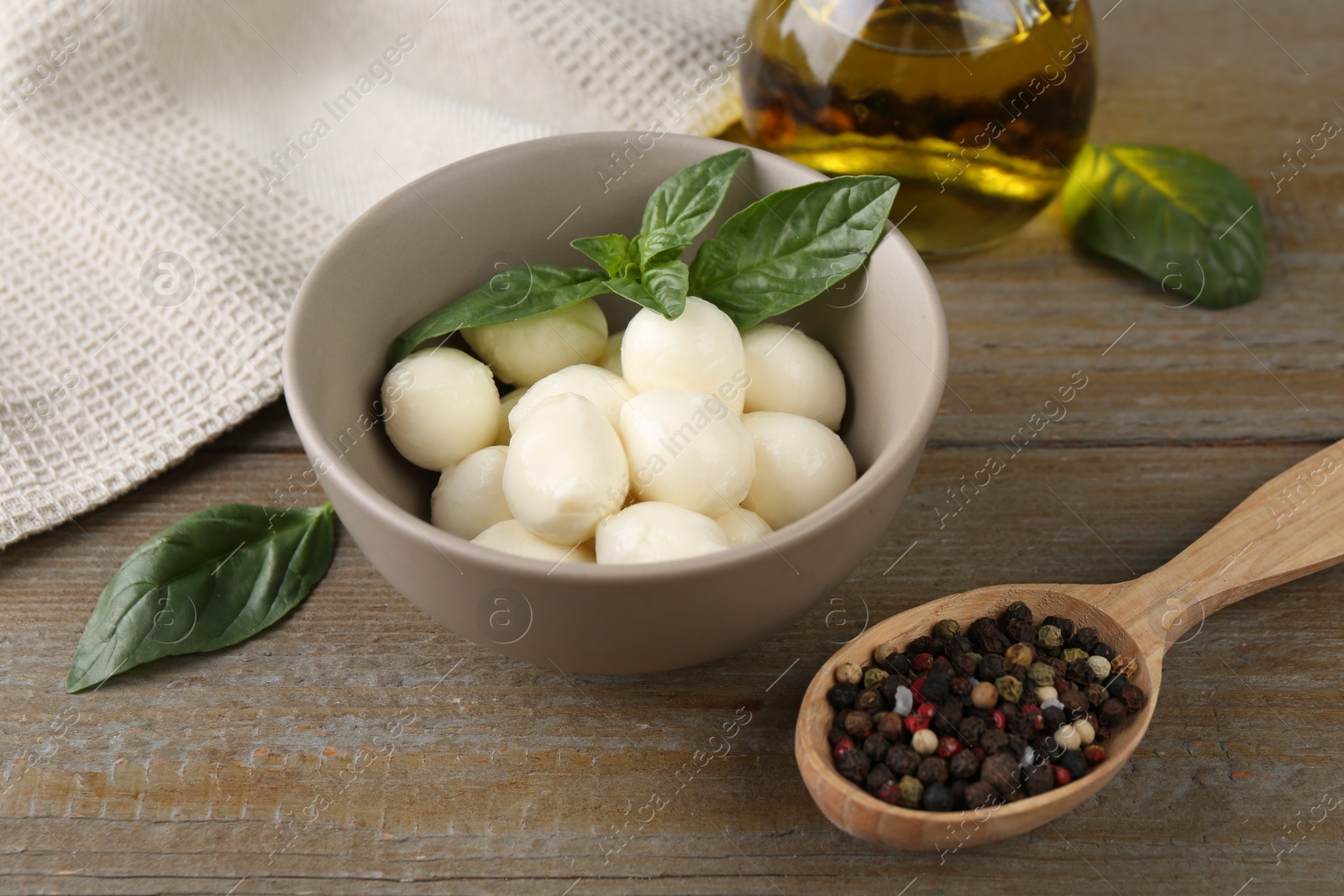 Photo of Tasty mozarella balls, basil leaves, oil and spices on wooden table